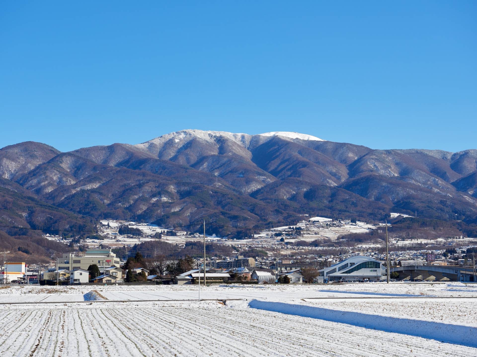 雪をかぶった北アルプスと松本の街並み
